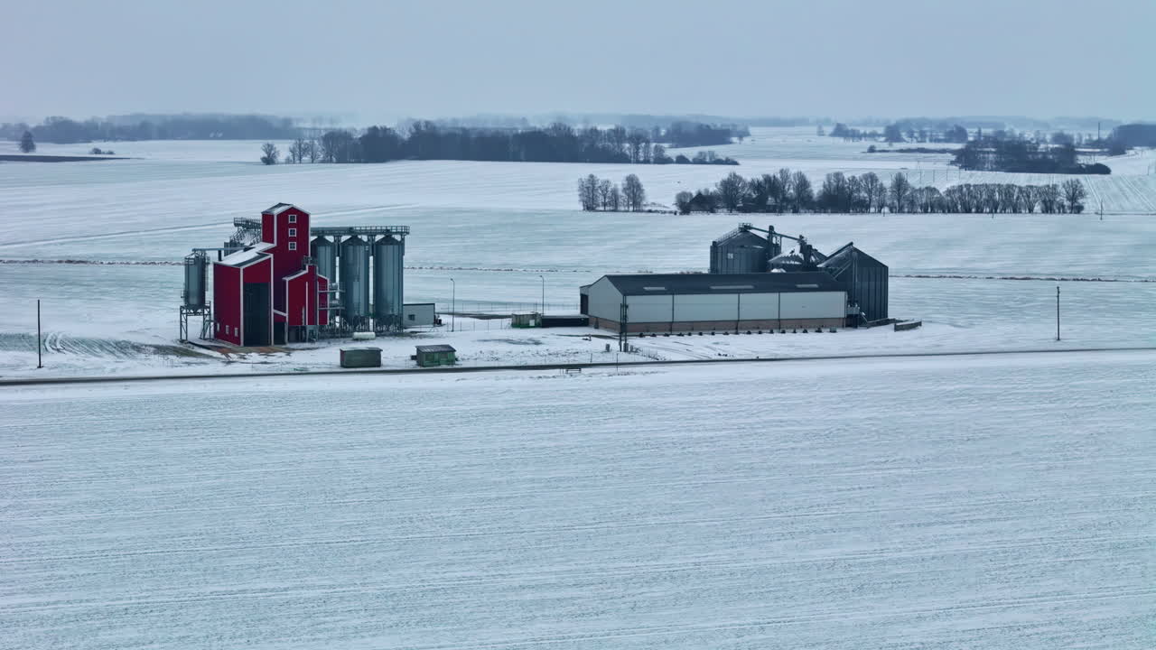 Snow covered farm buildings and silos surrounded by winter landscape, aerial