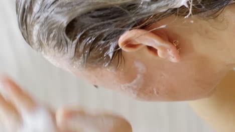 blonde girl washes her hair. white foam from shampoo on long hair. head hair care. vertical video
