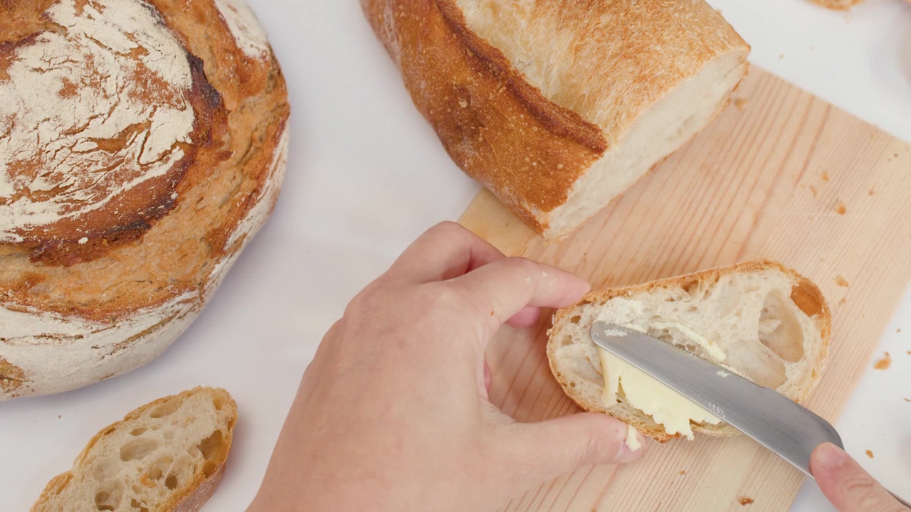 Close-up of hands scraping butter and spreading it onto crusty sourdough bread slices.