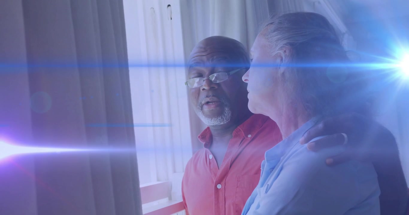 Man placing arm around woman offering support, gazing balcony door, lens flares sweeping in health