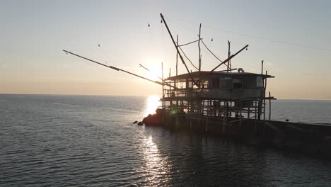 Vista-Aérea-Del-Paisaje-Marino-De-Una-Silueta-De-Trabucco,-Una-Máquina-De-Pesca-Tradicional,-En-La-Costa-Italiana,-Al-Atardecer