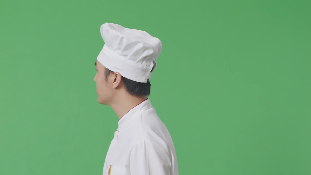 Vista laterale di uno chef asiatico che cammina e si guarda intorno in uno studio con sfondo green screen