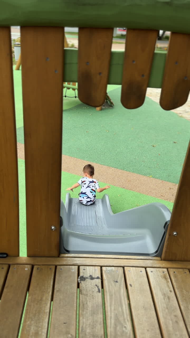 Rear view of a baby boy sliding at the playground. Kid slides down and turns to camera. Vertical video.