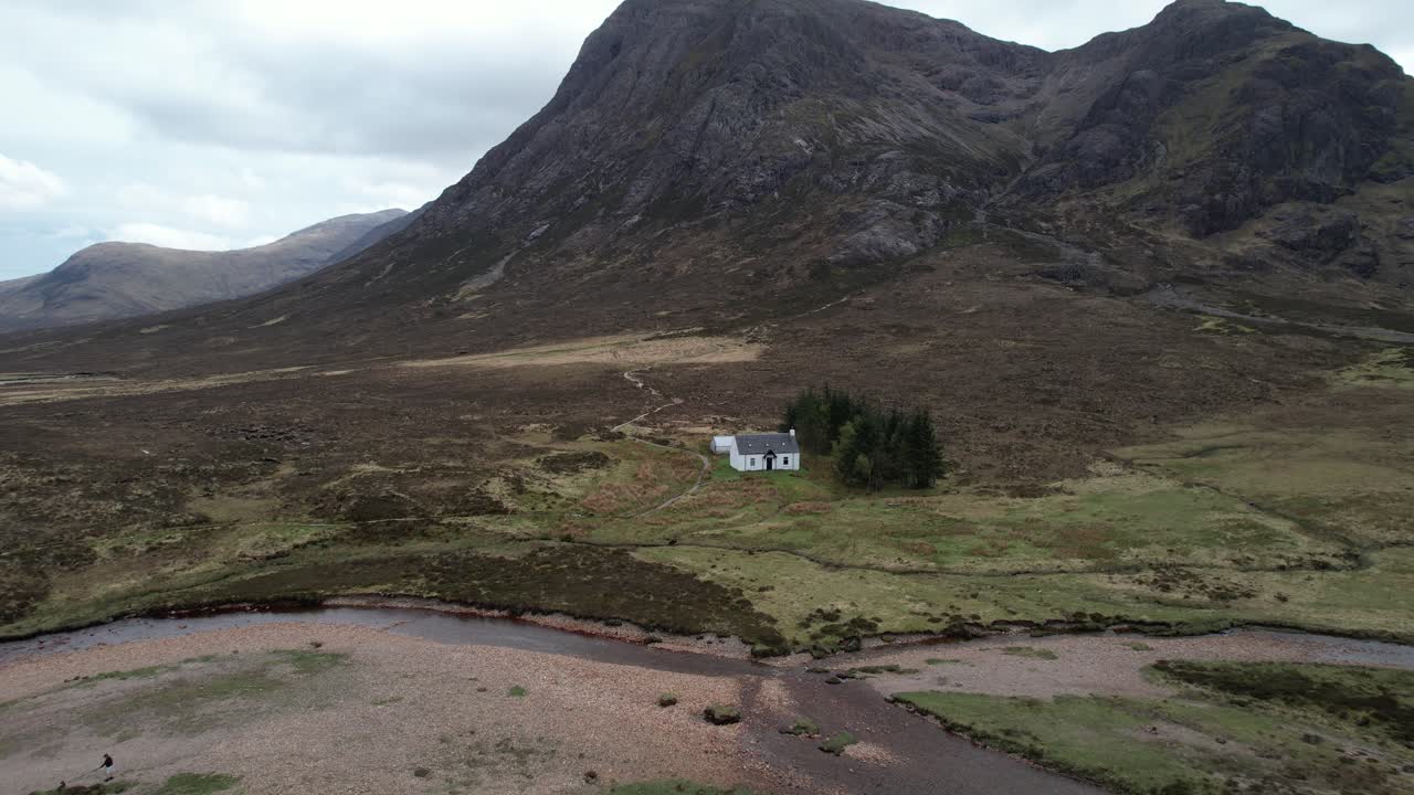 Cinematic pullback aerial shot of Glencoe Highlands with isolated white cottage in Scotland