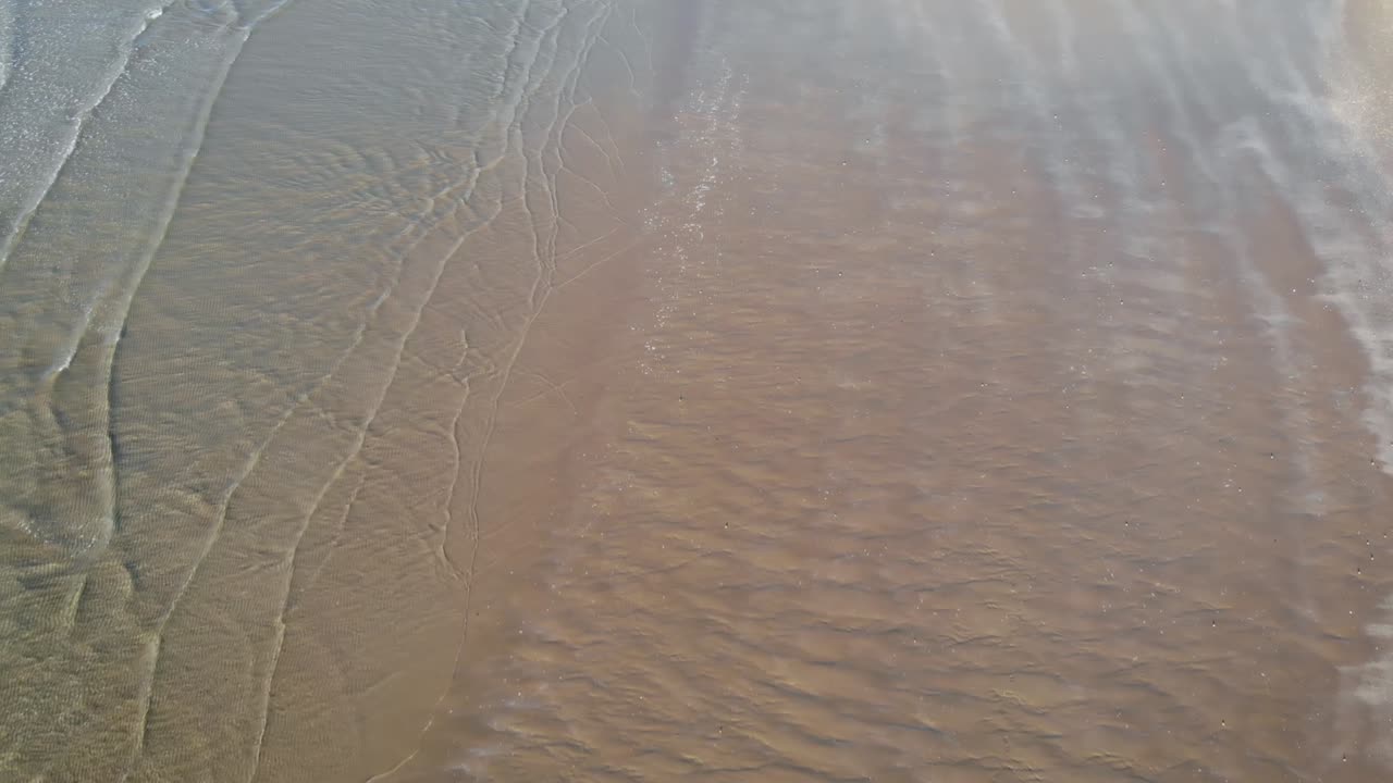 고요한 맑은 바다의 파도가 부드러운 대낮에 모래 해변을 부드럽게 덮습니다.