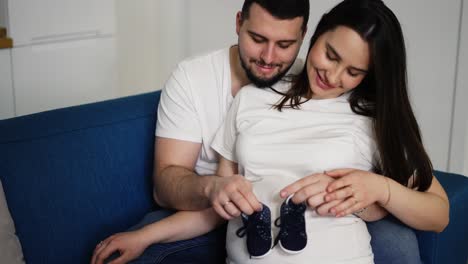 beautiful pregnant woman and her husband holding baby shoes on belly