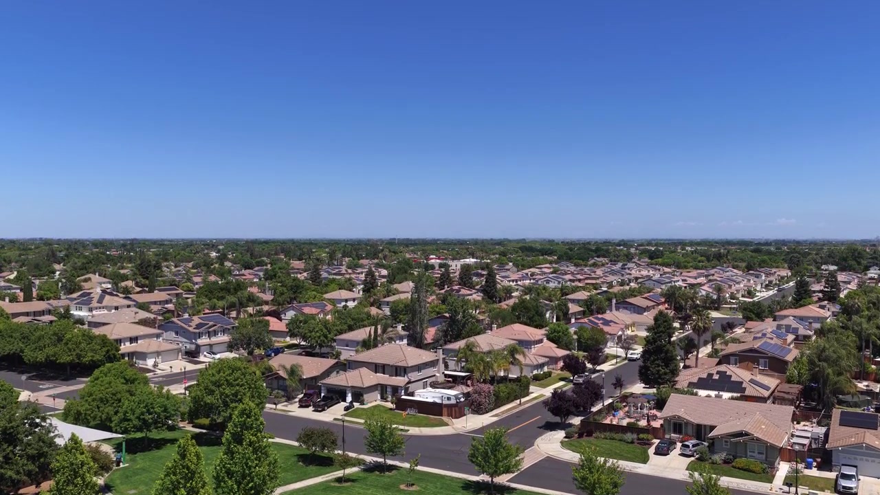 Yeşil bir parktan yükselerek Brentwood, Kaliforniya'da geniş bir banliyö mahallesini ortaya çıkaran, çatılar ve sokakların berrak mavi bir yaz gökyüzü altında sergilendiği bir drone perspektifi