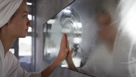 caucasian woman wipping the mist off the mirror in hotel