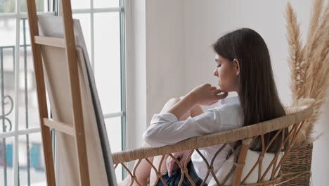 Una-Joven-Molesta-Mira-Por-La-Ventana-Sentada-En-Un-Estudio-De-Arte