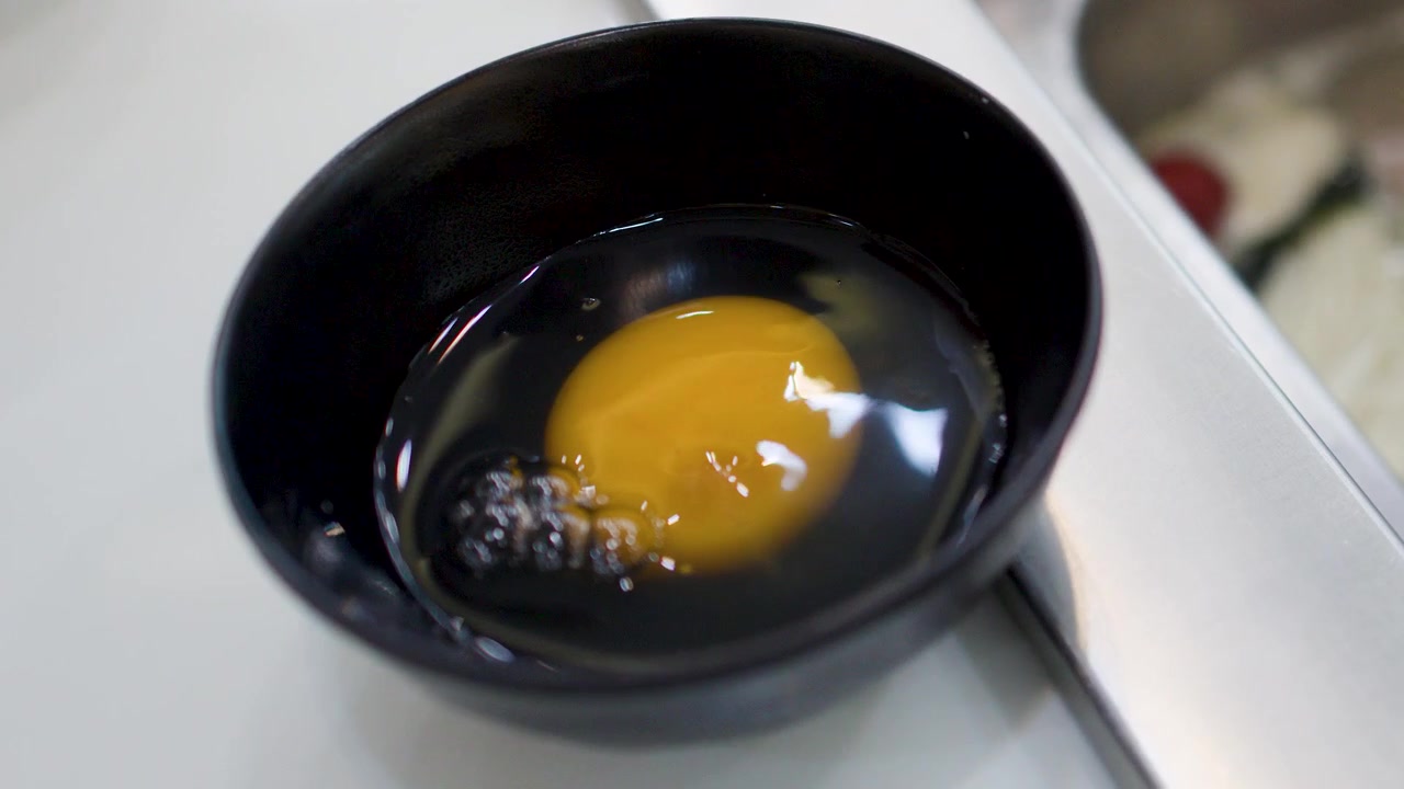 En person knekker et ferskt egg i en svart bolle til japansk shabu shabu-matlaging.