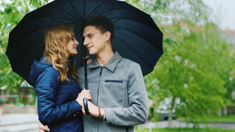 Junge-Frau-Und-Ein-Stylischer-Mann-Stehen-Auf-Der-Straße-Unter-Einem-Regenschirm-Es-Regnet