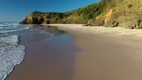 un hombre caminando por la playa de arena en la cabeza rota cerca de byron bay