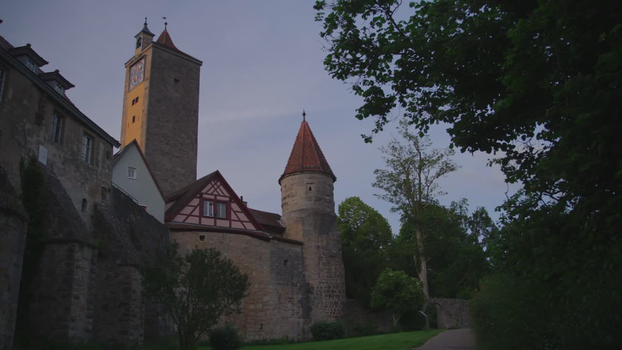Burgtor gate and surrounding stone structures in Rothenburg ob der Tauber, nestled among green foliage, showcasing remarkable historical architecture and a tranquil garden setting.
