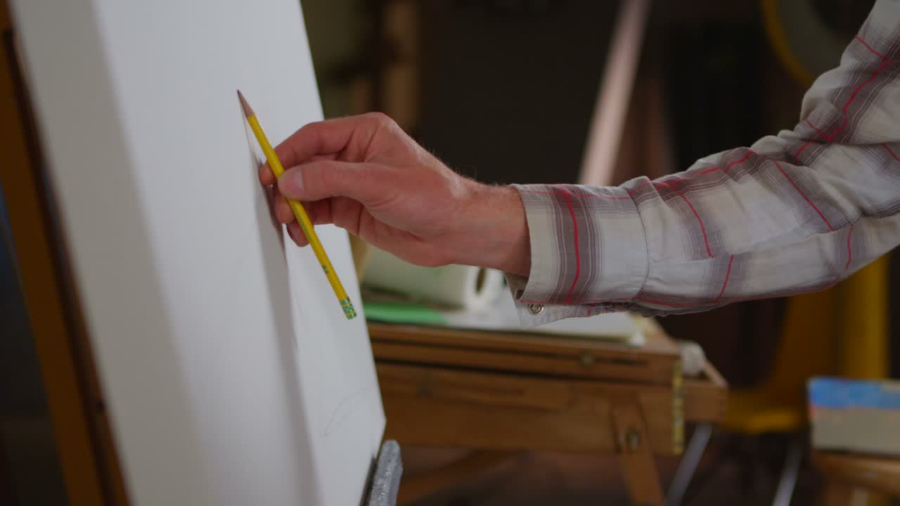 el primer plano de una mano cuando un artista comienza a dibujar en un lienzo en blanco