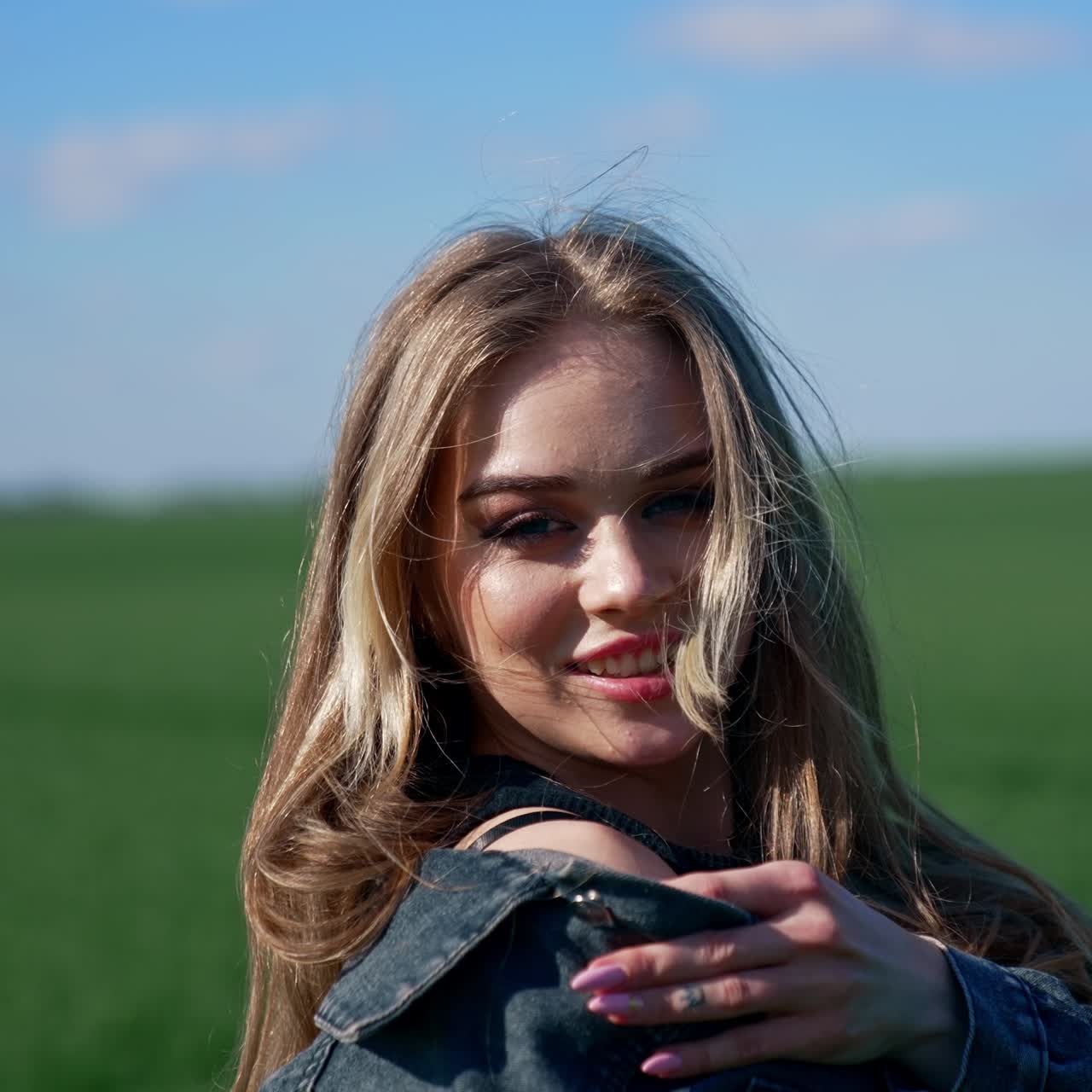 Happy girl on a meadow. Attractive young model with lovely face in denim suit posing on camera and smiles. Portrait of a young woman in nature in a sunny day