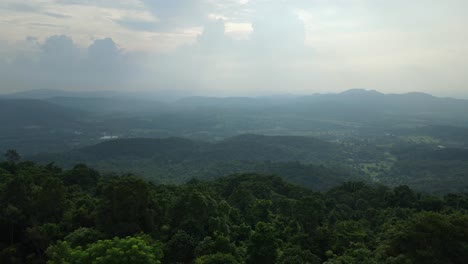 Aerial-ascending-footage-revealing-trees-in-foreground-in-the-mountain,-hills,-valley,-and-more-mountains-in-the-horizon-while-the-sun-is-setting