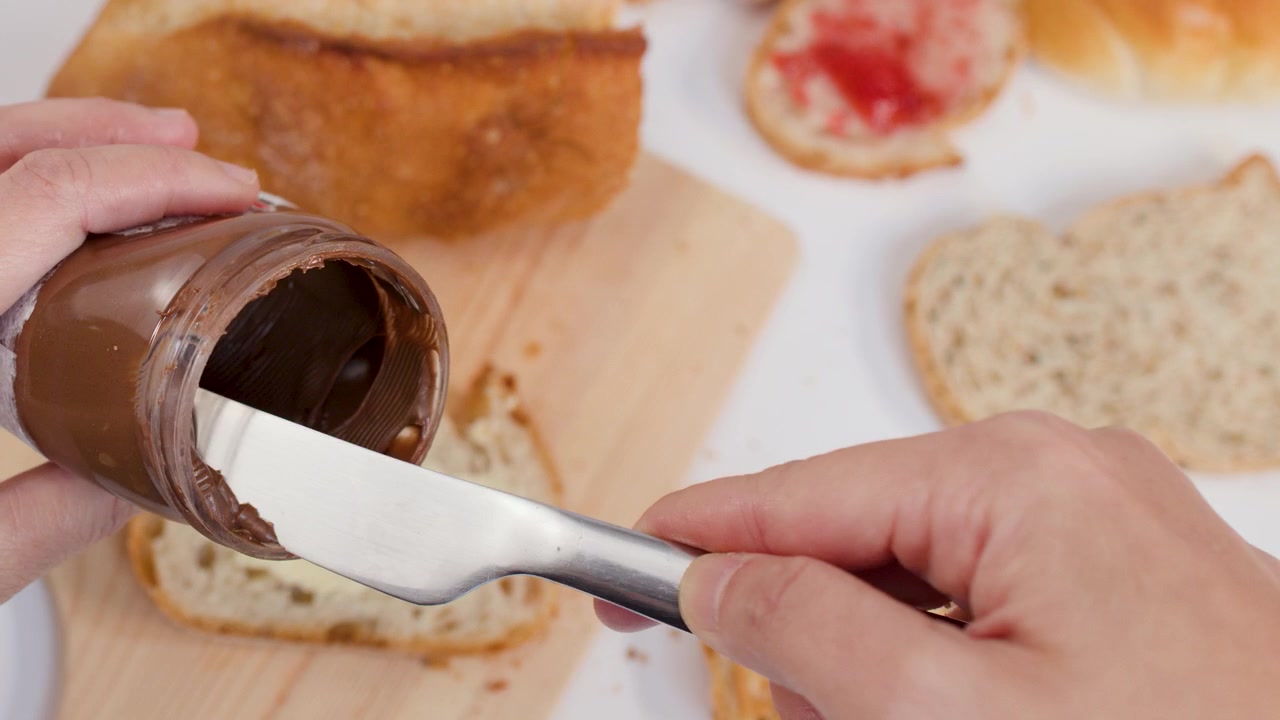 Vista dall'alto di mani che usano un coltello per spalmare crema al cioccolato sul pane tostato per la colazione.