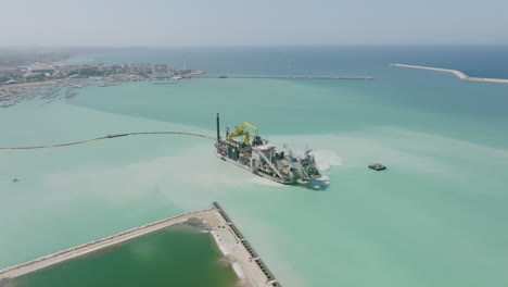 Wide-aerial-flyover-of-a-ship-that-is-dredging-up-sand-in-the-harbor-of-Bari,-Italy-during-the-daytime