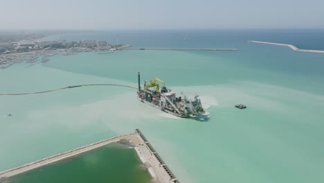 wide aerial flyover of a ship that is dredging up sand in the harbor of bari, italy during the daytime