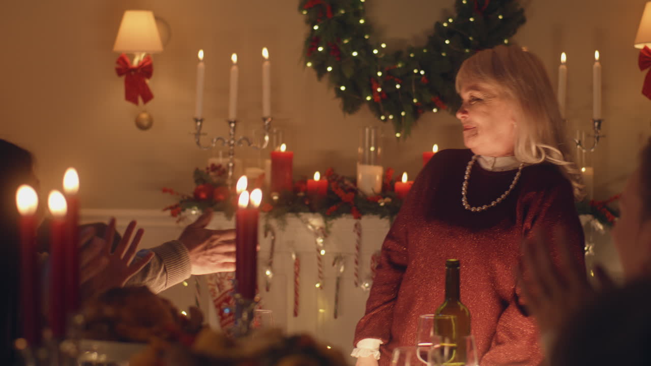 Grandmother Tells Joke at Family Christmas Dinner. Senior grandmother tells joke or life story to her large multi cultural family. They celebrating Christmas. Served table with dishes and candles. Warm atmosphere of family Christmas dinner at home