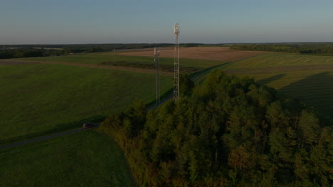 two cellular towers in the middle of farmland during sunrise, aerial dolly out tilting