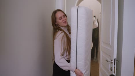 woman carrying a mattress in a hallway