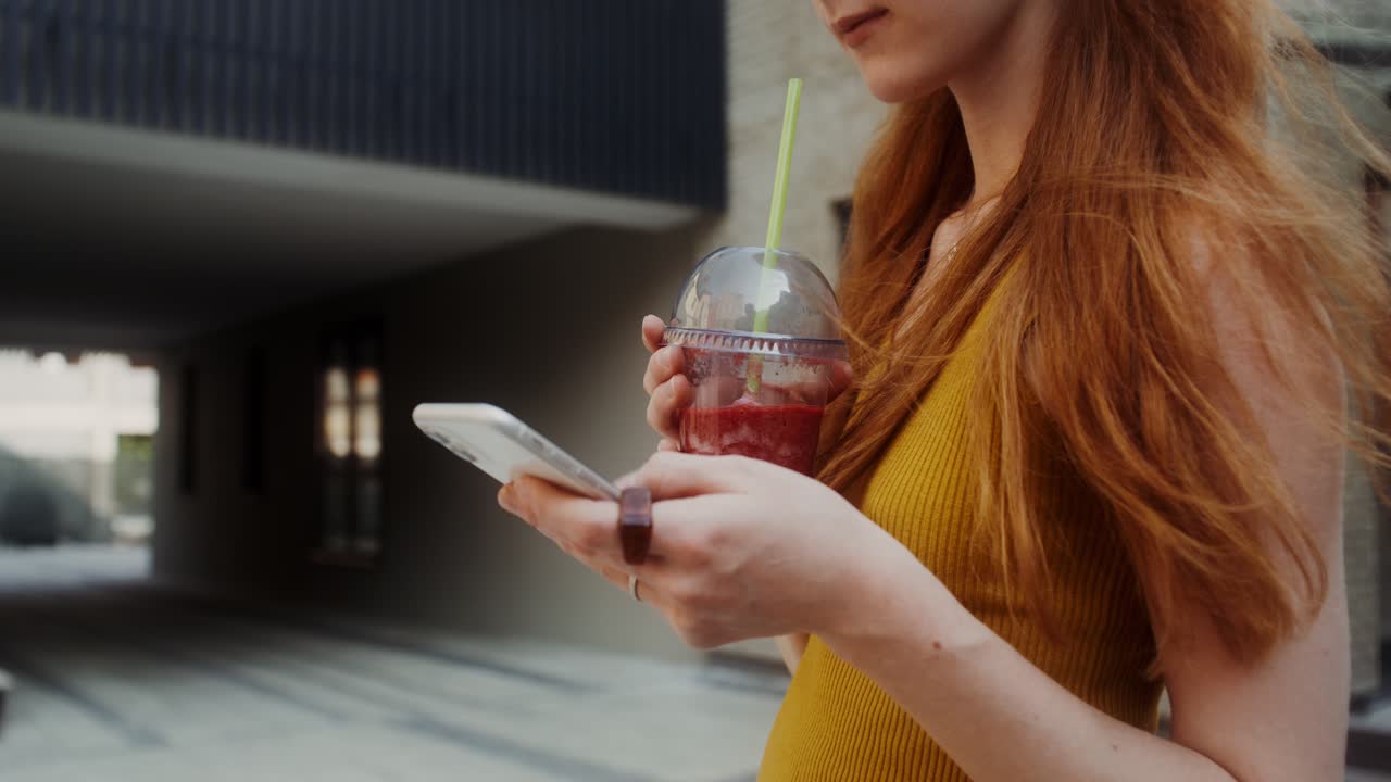 mujer joven bebiendo batido y usando el teléfono en la ciudad