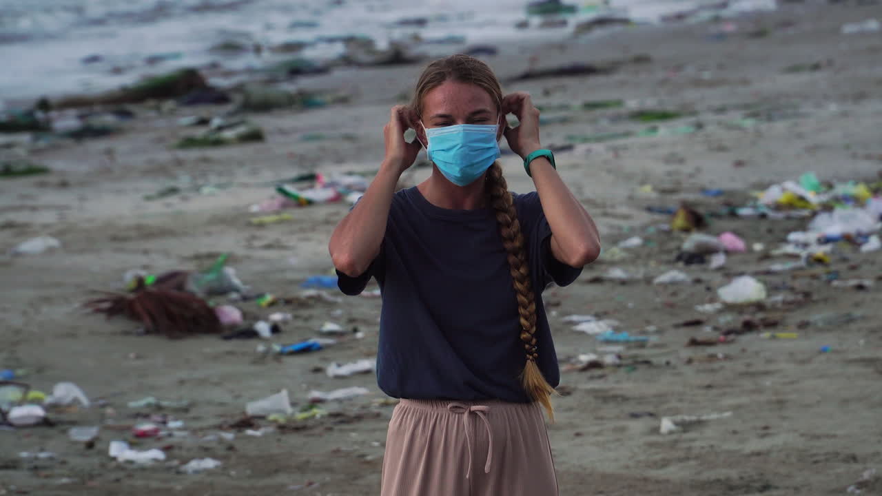 Woman Smile At Camera Then Wear A Face Mask While On The Beach With Trash