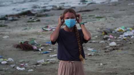 woman smile at camera then wear a face mask while on the beach with trash