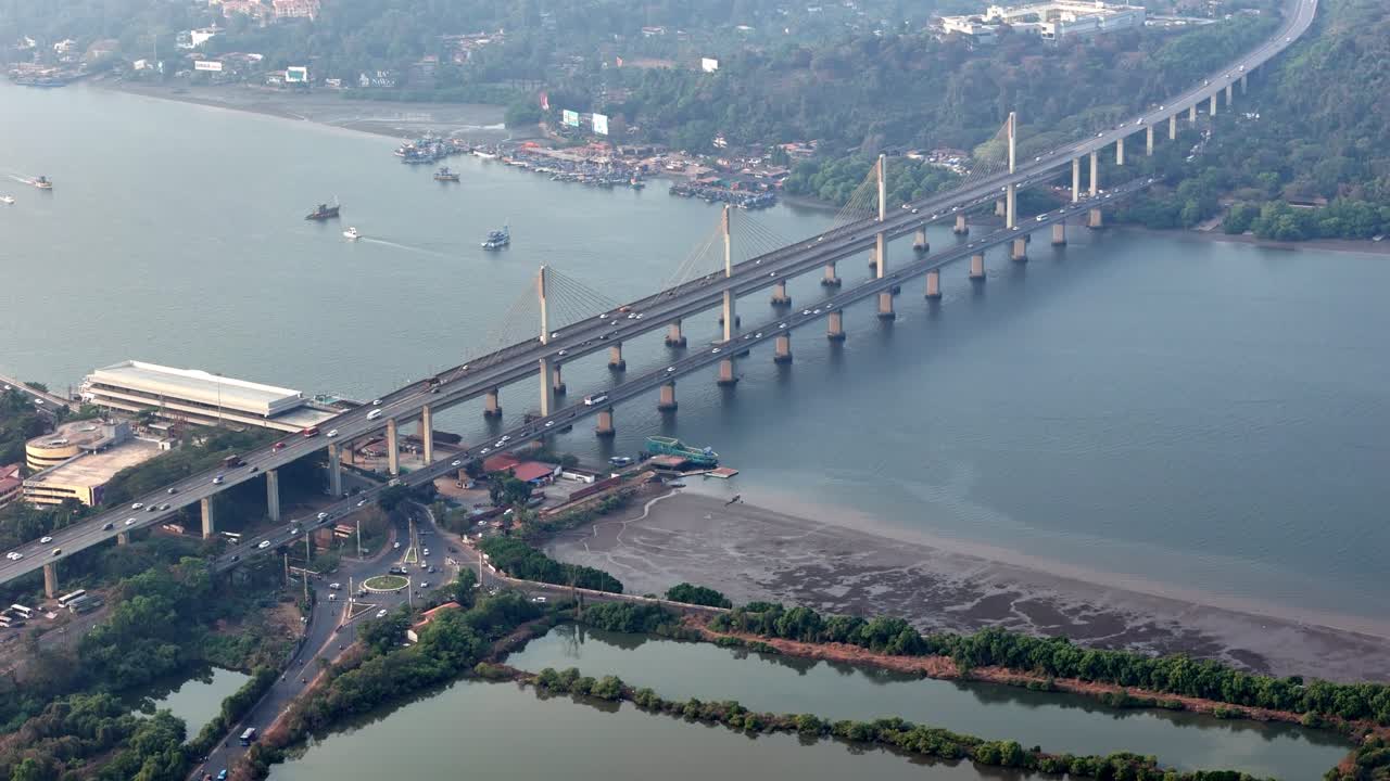 Ampia ripresa aerea dell'intero ponte Atal Setu che attraversa il sereno fiume Mandovi, con cavi strutturati, traffico in movimento e dintorni panoramici che creano un equilibrio tra ingegneria e natura