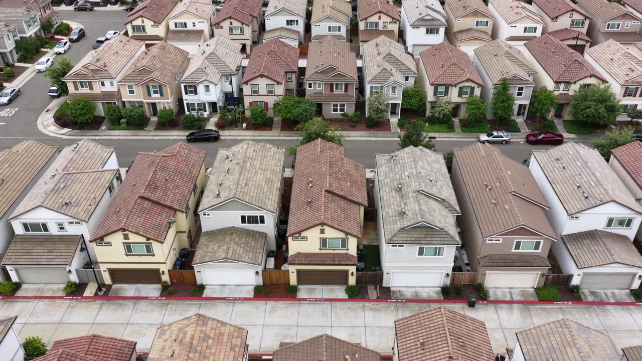 Tætpakkede rækker af stuk-huse med matchende tegltage i terrakotta, tilhørende garager og små haver fylder forstadsgaderne i Rancho Cordova, Californien, USA. Dronebillede oppefra.