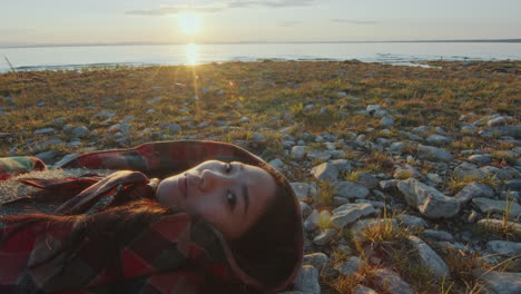 retrato de una mujer joven acostada en una orilla rocosa durante la puesta de sol de la hora dorada