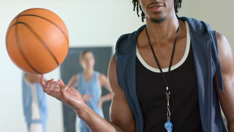 spinning basketball on finger, coach wearing whistle standing in gym with players