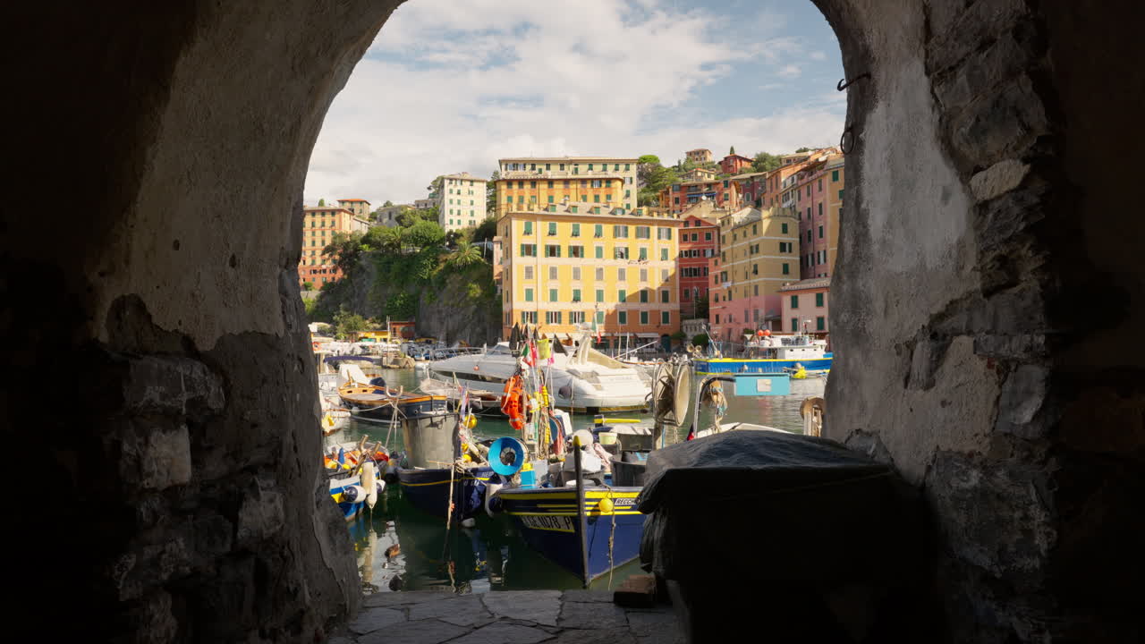 Turisti a piedi nel colorato porto di Camogli visto attraverso un arco storico in pietra