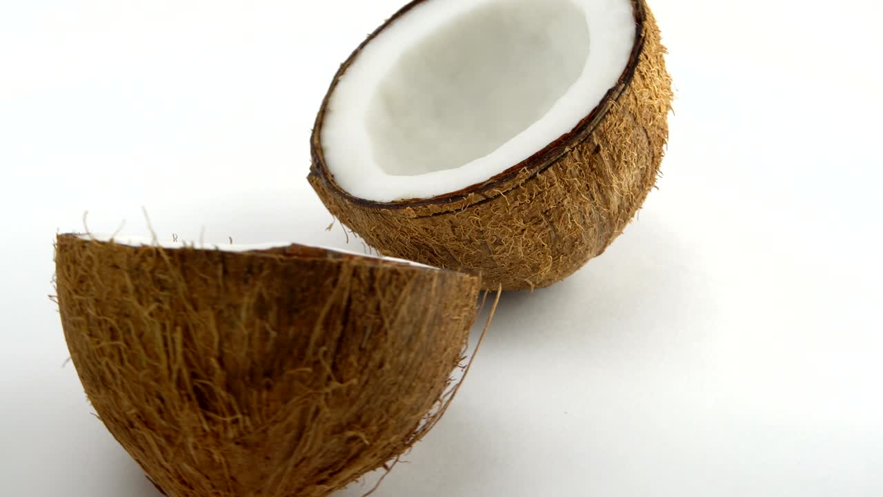 coco tropical maduro dividido en dos mitades girando sobre un fondo blanco. frutas tropicales. en bucle