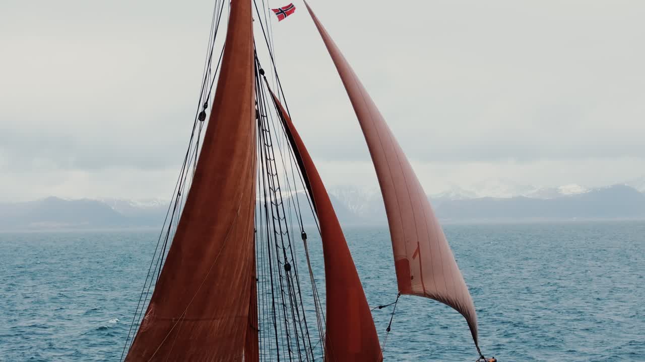 Nærbillede fra drone af sejlbådssejl fyldt med vind, varmtonet lærred mod overskyet himmel, detaljeret rigning og mast, koncept for maritimt eventyr og sejlads.