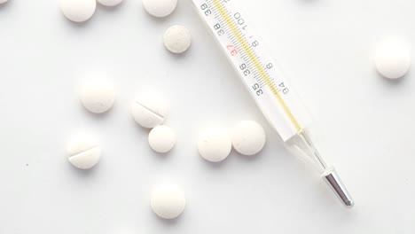 thermometer and pills on a white surface