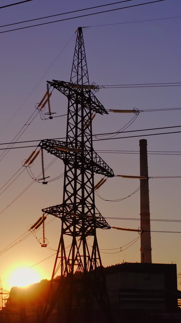Electricity pylons and lines at dusk. Silhouette of high voltage tower and wires. Vertical video