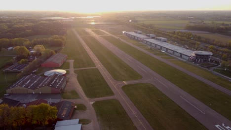 Toma-Aérea-De-Elevación-De-Una-Pista-De-Aterrizaje-En-Un-Aeropuerto-Durante-La-Puesta-De-Sol-En-Los-Países-Bajos