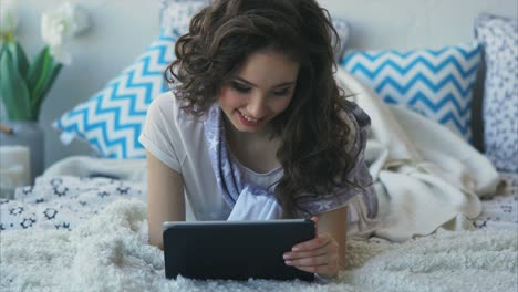 young woman relaxing on a bed with a tablet
