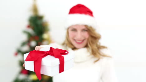 una rubia festiva sonriendo a la cámara ofreciendo un regalo.