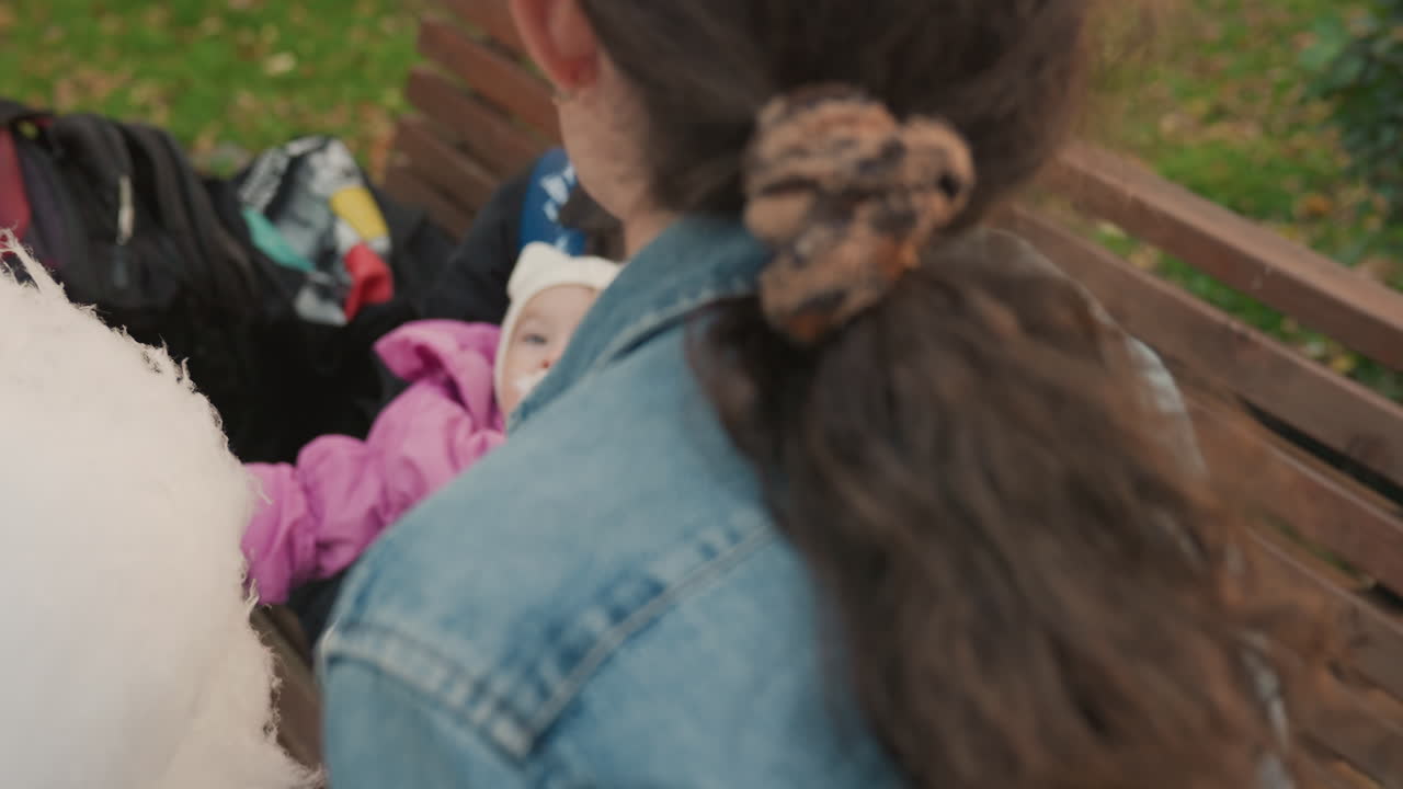 Giovani genitori bianchi con il bambino che assaggia lo zucchero filato su una panchina del parco, la madre stacca un pezzettino e lo offre al neonato in un completino rosa, padre che tiene in braccio il bambino, interazione familiare calda e premurosa, intimo.