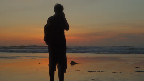 Fotógrafo-De-Silueta-Tomando-Fotos-De-La-Playa-Al-Atardecer,-Revelación-Lenta