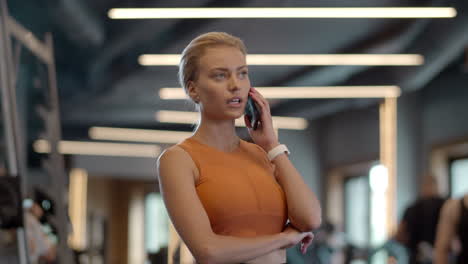 focused sportswoman talking on phone at gym. athlete girl standing in sport club