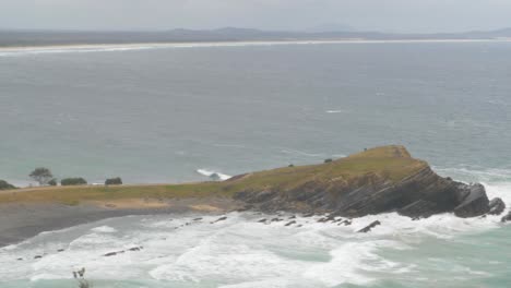 Mädchen,-Das-An-Einem-Windigen-Morgen-Die-Arme-In-Die-Luft-Hebt-Und-Streckt---Kiesstrand-Und-Halbinsel-Am-Crescent-Head,-Nsw,-Australien