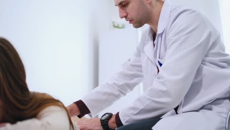 male doctor diagnoses woman's spine. physiotherapist is doing check up of patient's back in clinic. female patient lying on medical bed. health care concept.