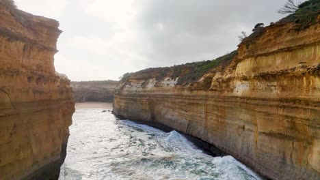 aerial footage of rugged cliffs and ocean waves at loch ard gorge, port campbell, australia. overcast lighting enhances the dramatic landscape