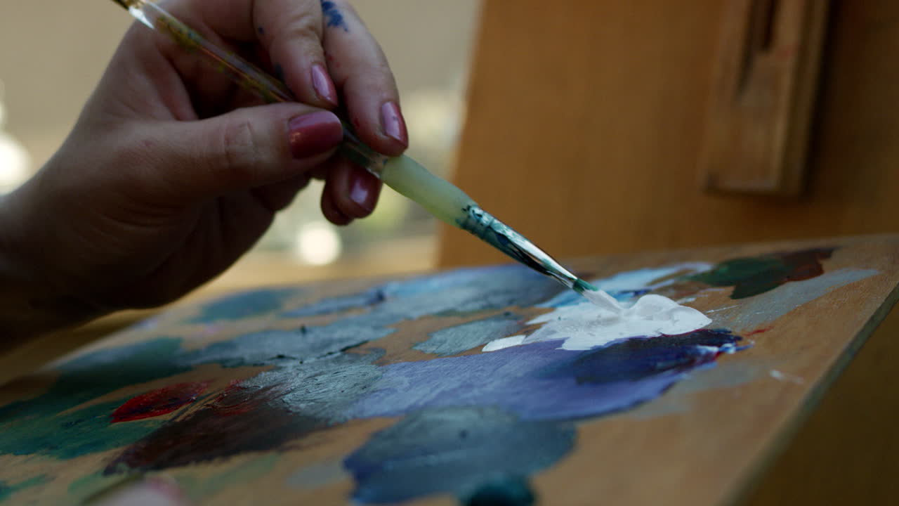 SLOW MOTION video of artist applying white paint to brush then canvas