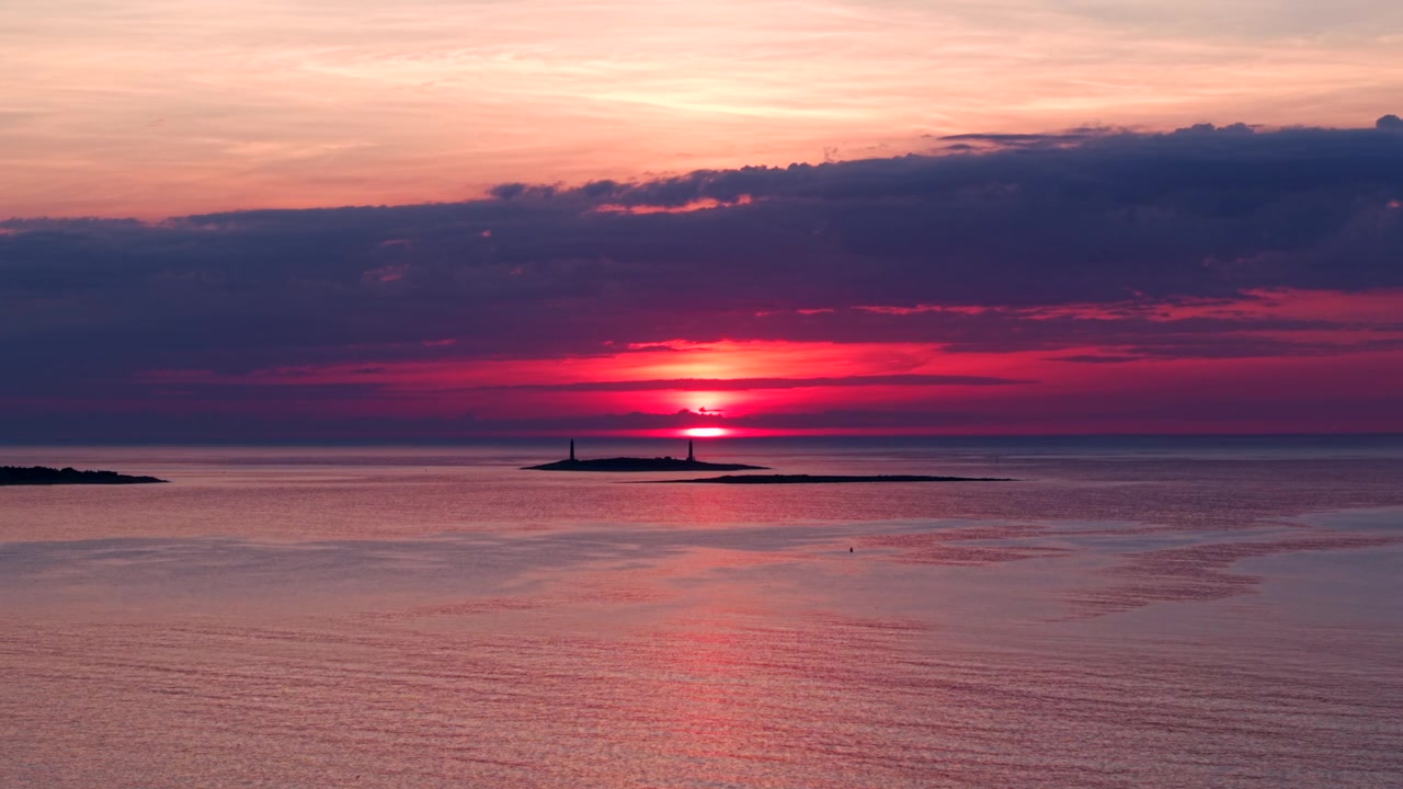 Vue aérienne des deux phares jumeaux de l'île Thacher se découpant à l'aube à Rockport, MA. Des nuages roses, violets et oranges se reflètent sur l'eau calme de l'océan. Paysage grand angle et cinématographique. Personne.