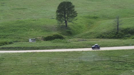 航空侧视图,一辆4x4吉普车在公路旅行中,在铺设的道路上行驶,周围的绿草田山丘